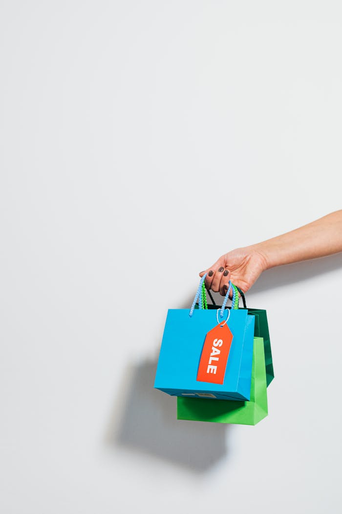 A hand holding colorful shopping bags with a prominent sale tag, conveying a retail discount theme.