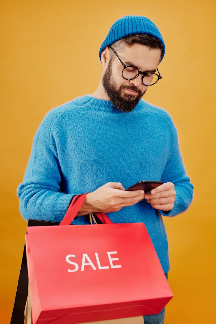 Bearded man wearing blue sweater and beanie shopping during sale while using smartphone.